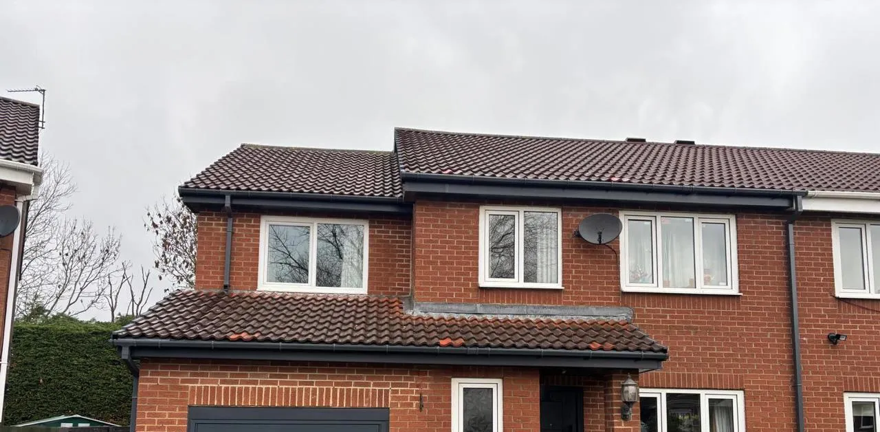 Semi-detached brick house in Jarrow after roofline replacement, showing new anthracite fascias, soffits and guttering along the roof edge.